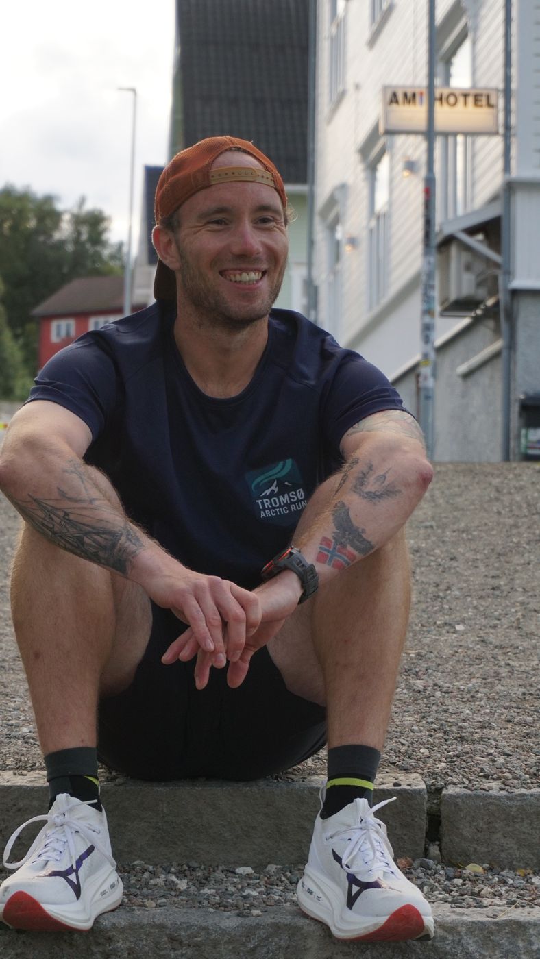 Kristoffer, founder and guide of Tromsø Arctic Run, sitting relaxed on a step in Tromsø and smiling