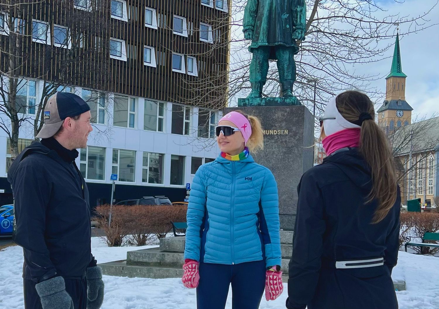 A guide in conversation with two guests in winter clothes in front of the Roald Amundsen statue in Tromsø