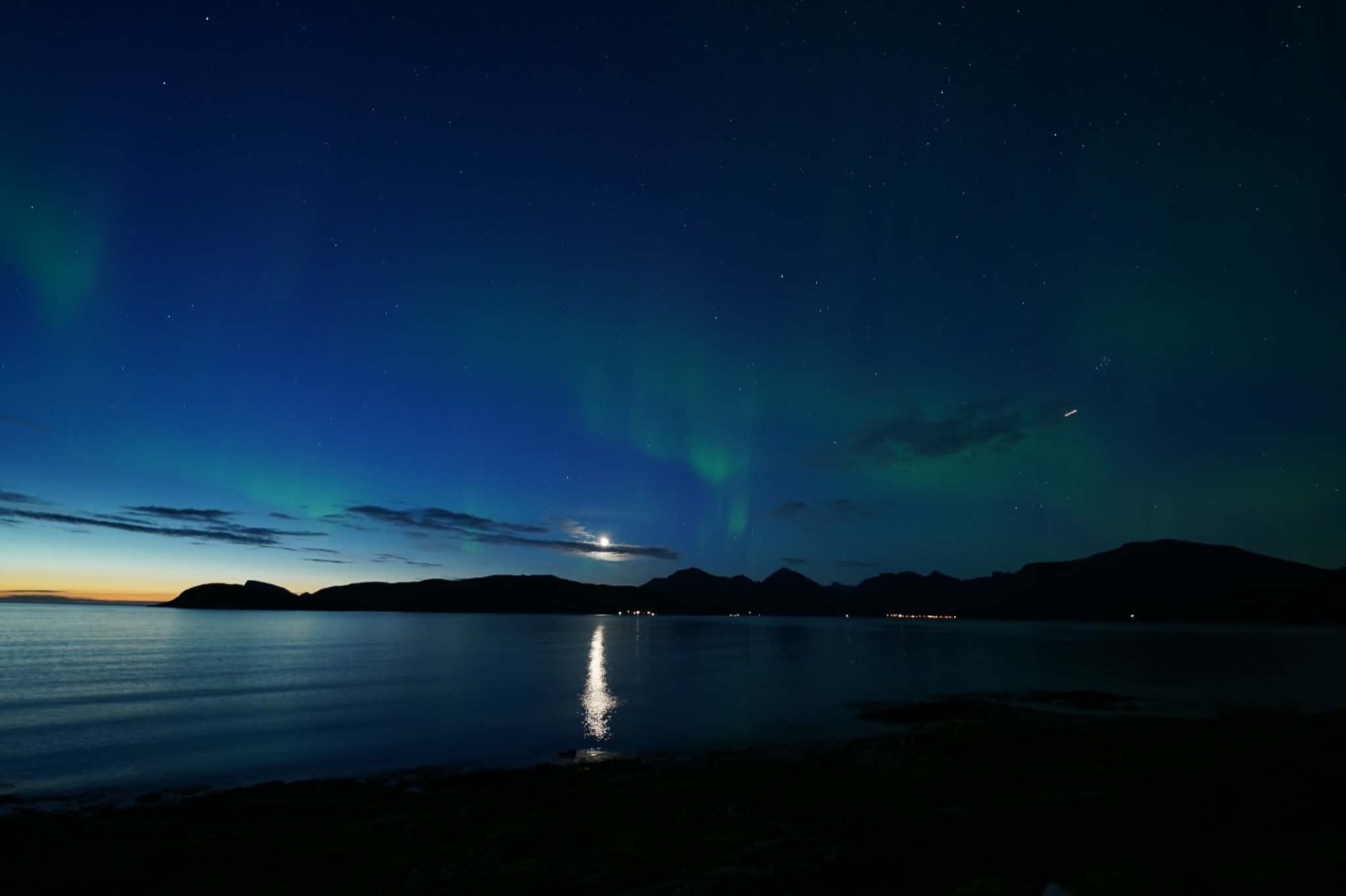 Aurora, a crescent moon and a shooting star over a Tromsø fjord