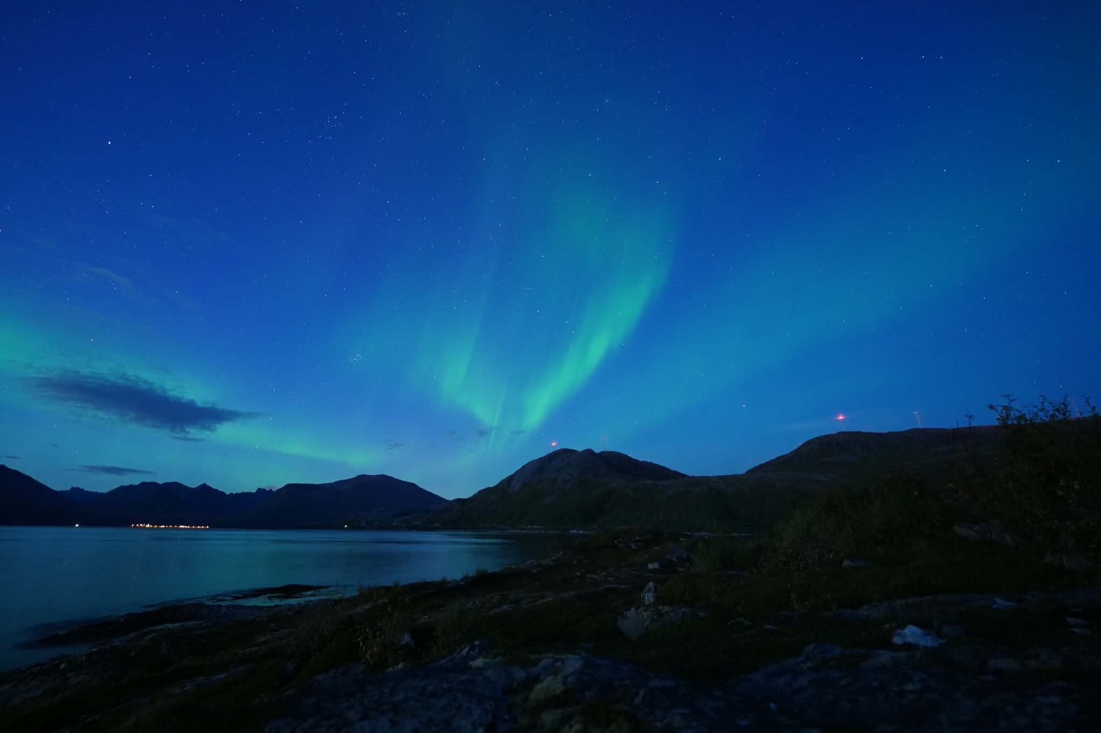 Green northern lights rising above a dark fjord and mountains near Tromsø