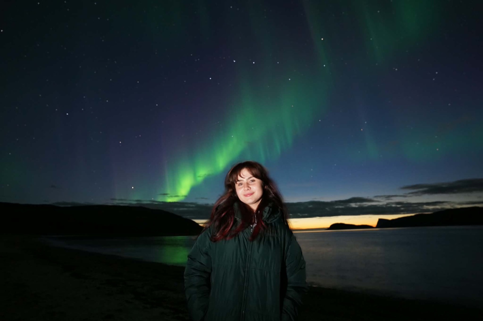 A guest smiling with the northern lights overhead