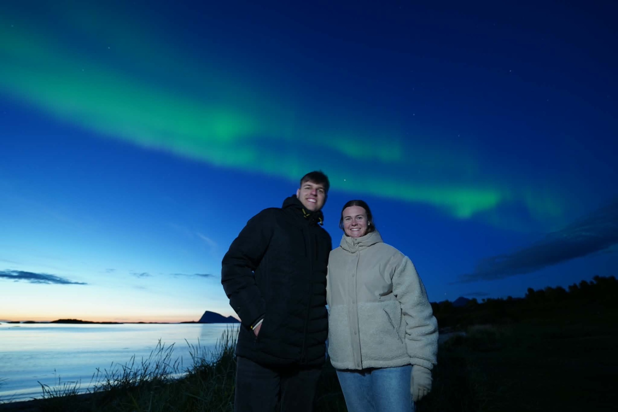 Guests watching the northern lights over a fjord on a Snow Travels tour