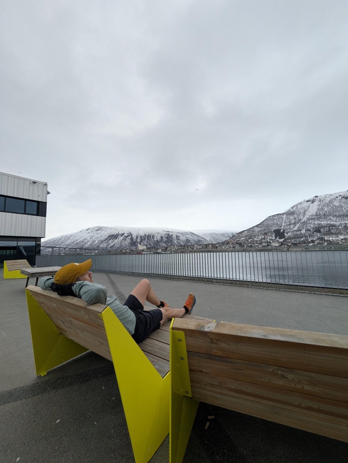 Kristoffer resting on a bench above Tromsø with the fjord and snow-capped mountains behind him